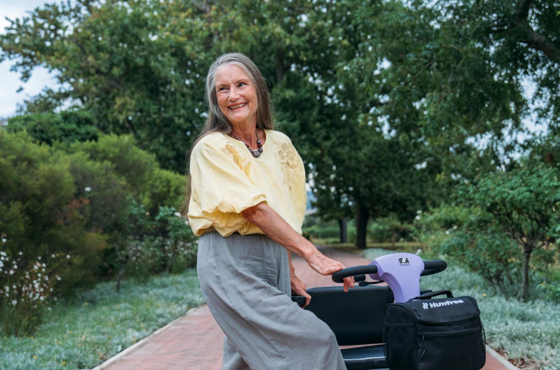 Woman dressed in yellow top and grey trousers, standing next to a Humfree Connect scooter in Amethyst