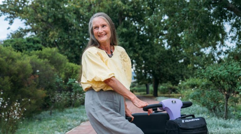 Woman dressed in yellow top and grey trousers, standing next to a Humfree Connect scooter in Amethyst