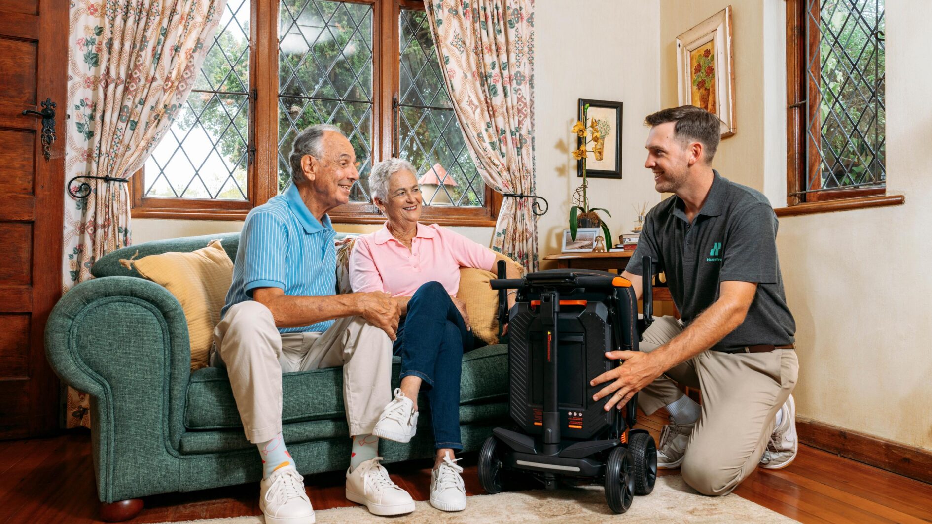 Older couple enjoying a carbon scooter demonstration in their living room with a humfree mobility expert