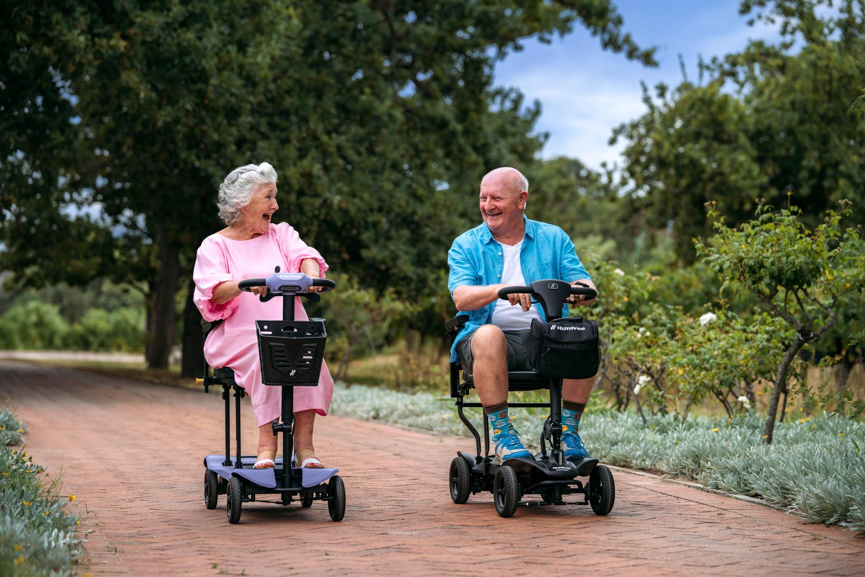 Older couple laughing as they ride a Humfree lite in amethyst and a Humfree connect in charcoal in the park
