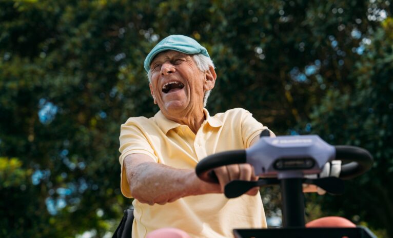 Close up of older man wearing a yellow shirt and pink trousers laughing as he rides amethyst Humfree lite scooter
